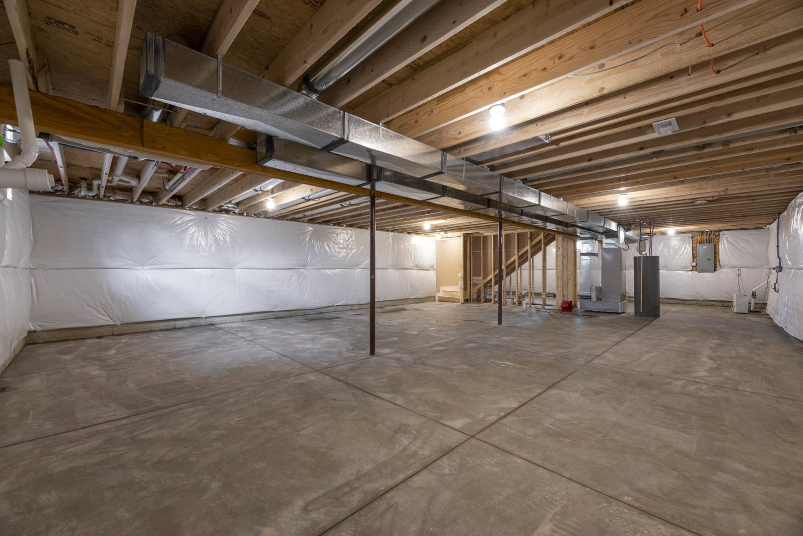 Concrete floor with white covering, exposed metal pipes on ceiling, white plastic wall covering, blurry ceiling light, black object with brown stripe near wall.
