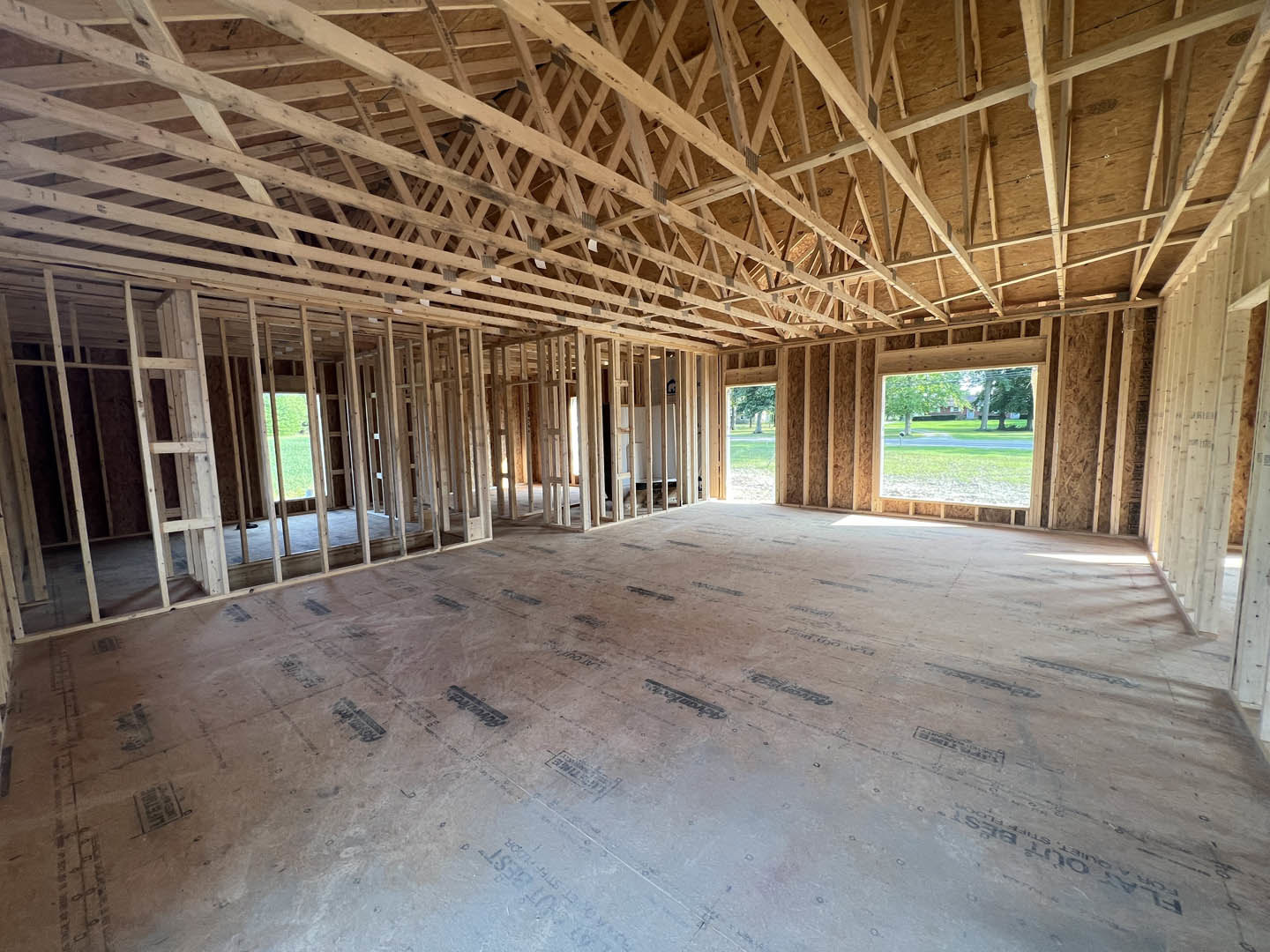 Exposed wood ceiling beams, large window overlooking grassy field and road, light-colored walls, unfinished floor