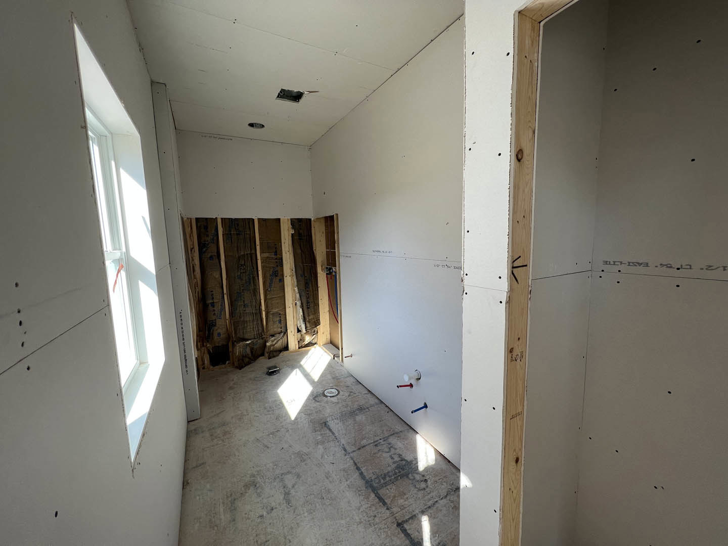Unfinished room with plaster walls, concrete floor, white cabinet, white door, window marked with red tape, and visible holes in wall