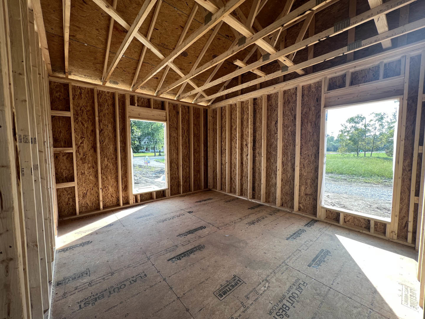 Vaulted ceiling with exposed wood beams, large windows overlooking a grassy field, light walls, and hardwood flooring