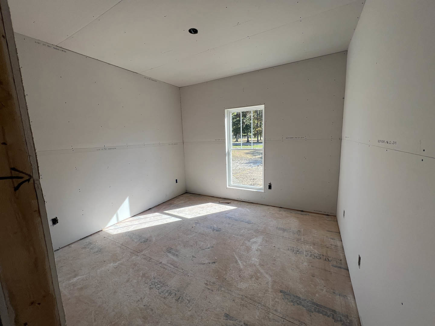 Concrete floor room with white plaster walls, large window overlooking trees and grass, ceiling hole, and black line detail on stone surface