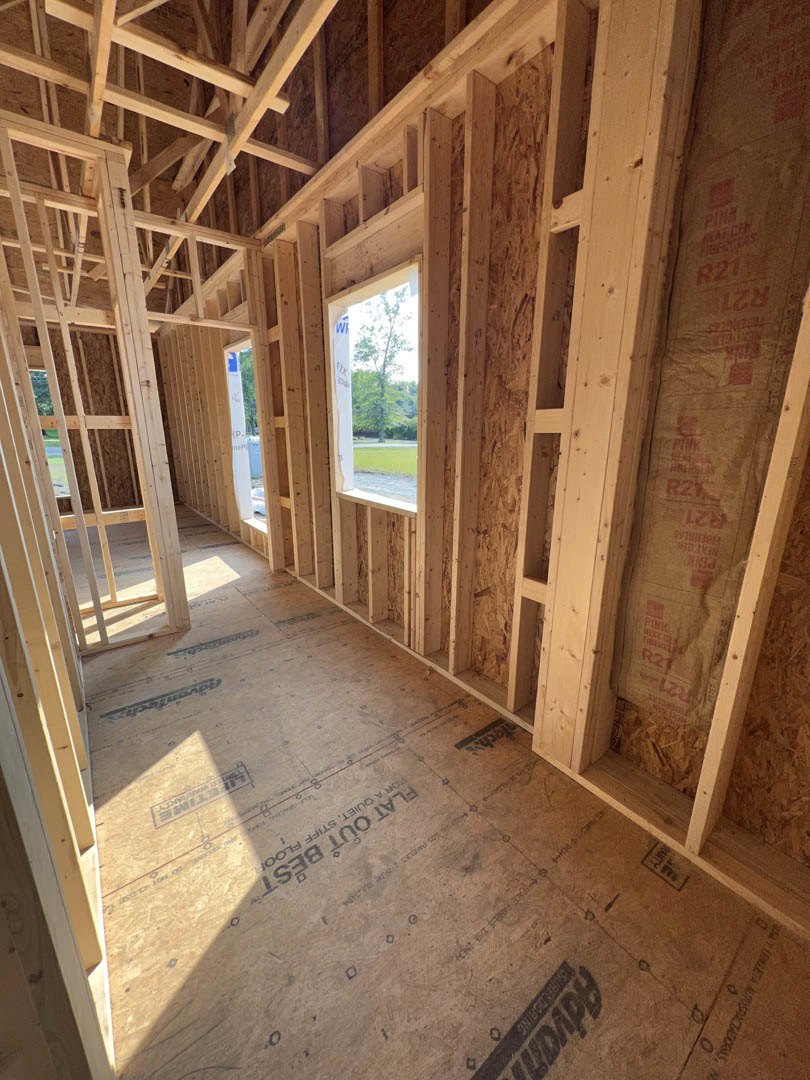Exposed wood framing and beams in a partially constructed room, window with a sign, unfinished floor, and visible construction materials