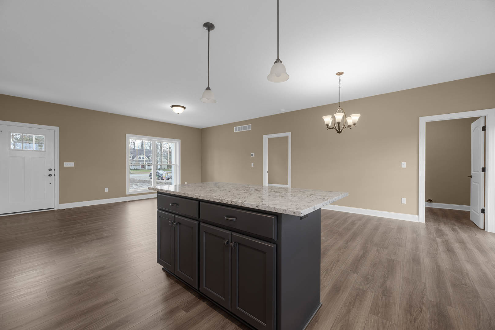 Marble kitchen island with white cabinetry, laminate flooring, chandelier overhead, white door with window, brown accent wall, and large window showing neighboring house