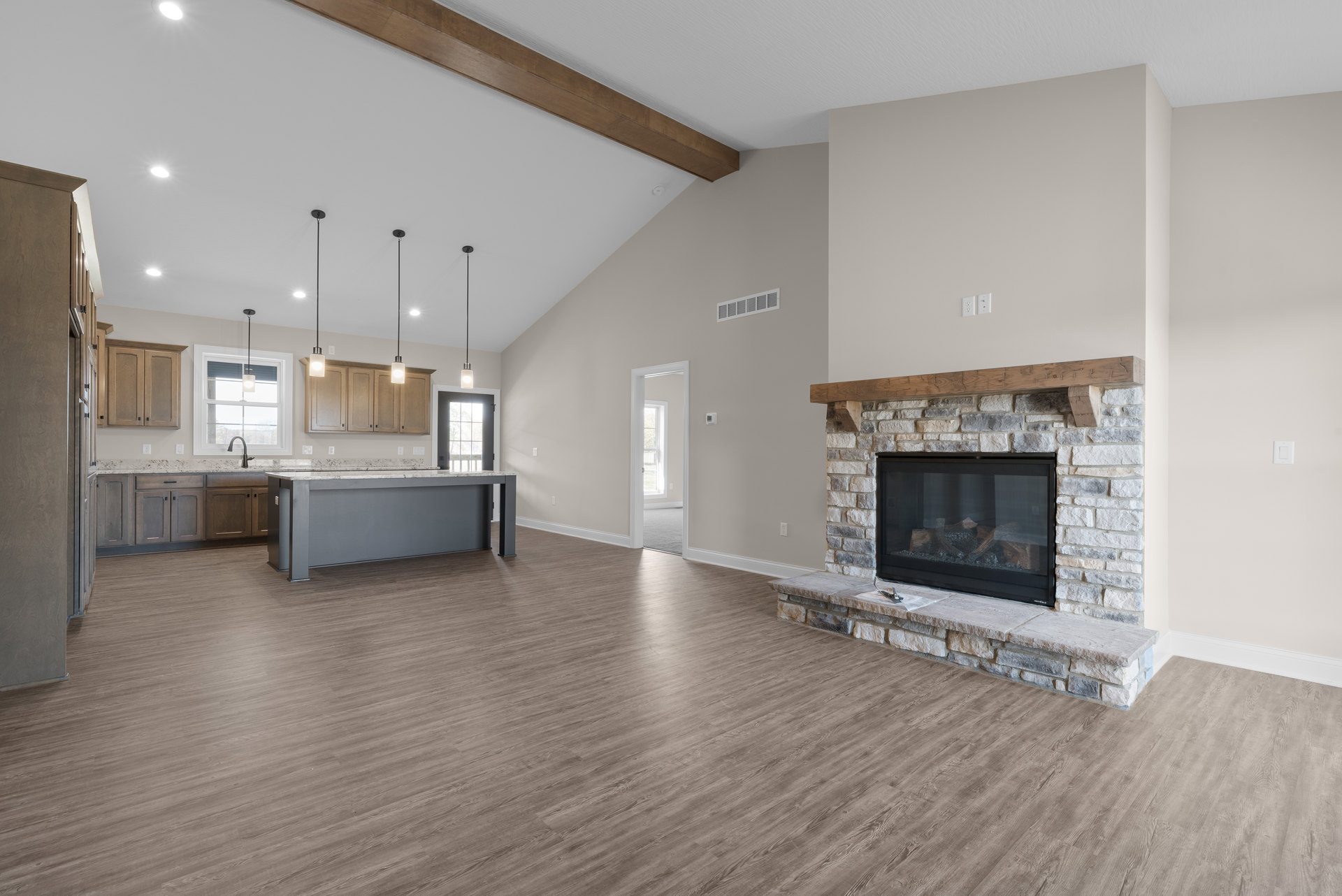 Living room with wood flooring, white fireplace featuring a wood mantle and glass door, open kitchen with grey cabinetry and marble countertops, white door with glass panes