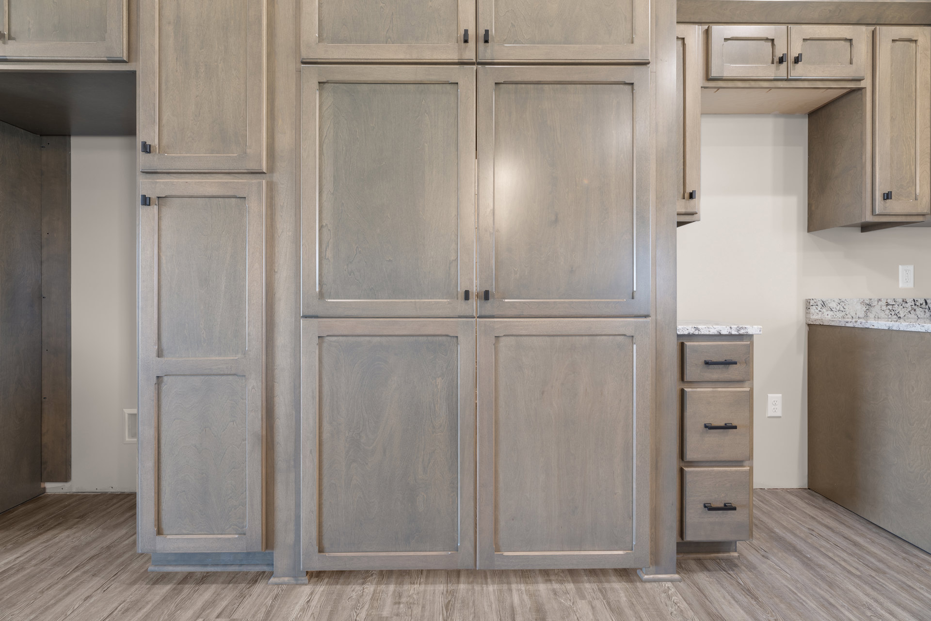 Large wood kitchen cabinet with silver trim, granite countertop, and built-in drawers, set against a light-colored wall.