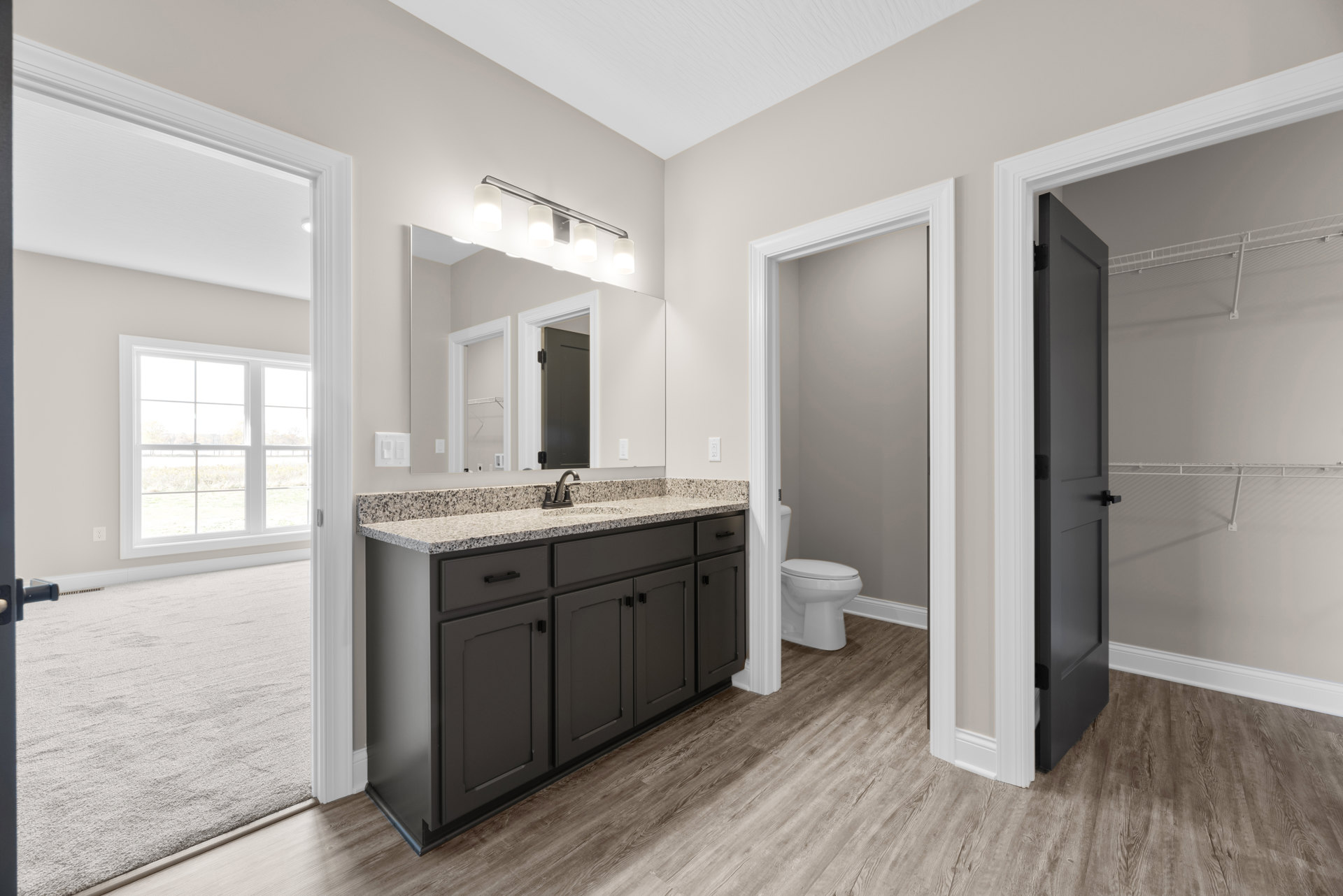 Bathroom featuring a marble countertop with undermount sink, chrome faucet, white toilet, tile flooring, and a window overlooking a grassy field.