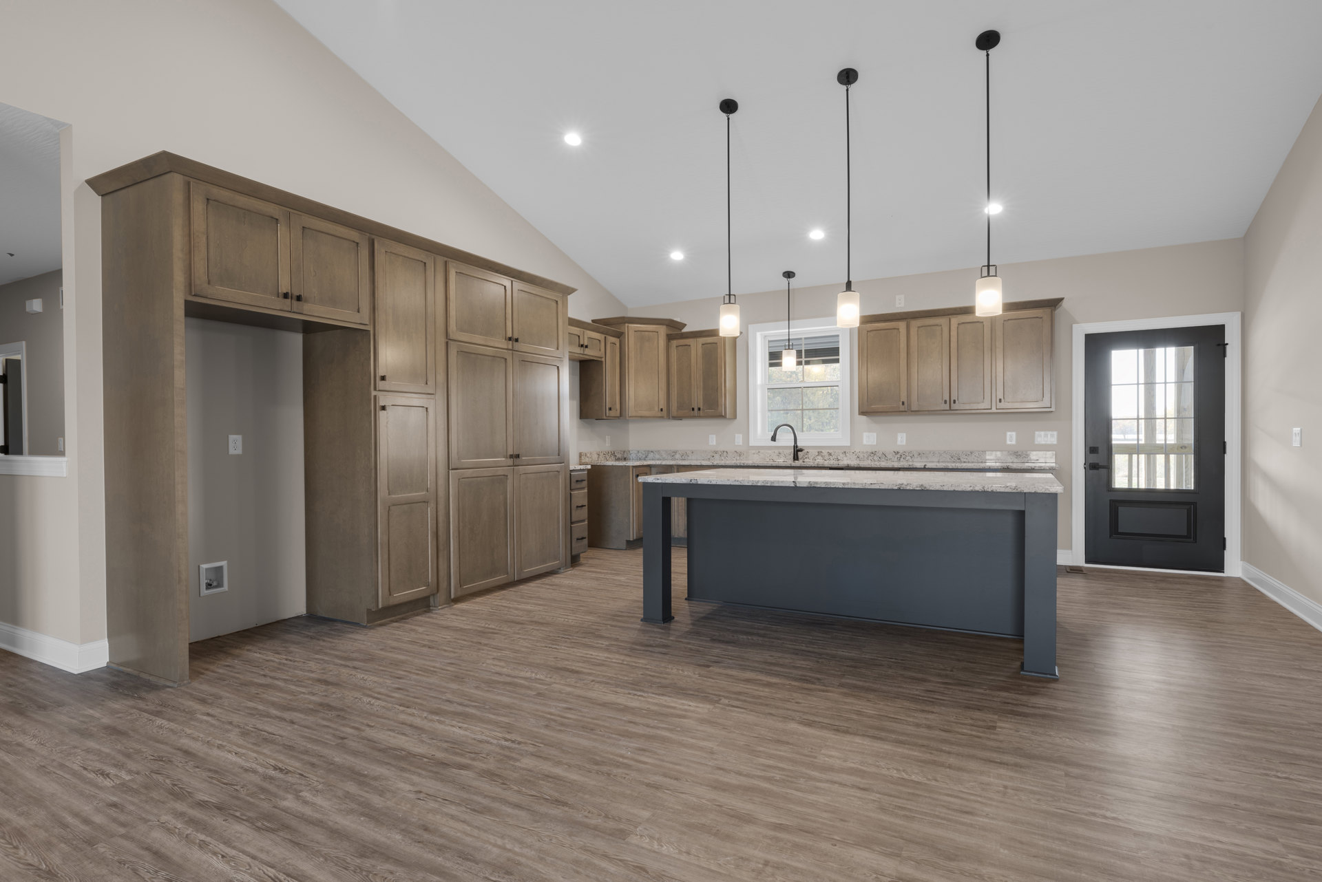 Spacious kitchen featuring a large central island with built-in sink, wood flooring, white cabinetry, ceiling light fixture, and a door with a window.