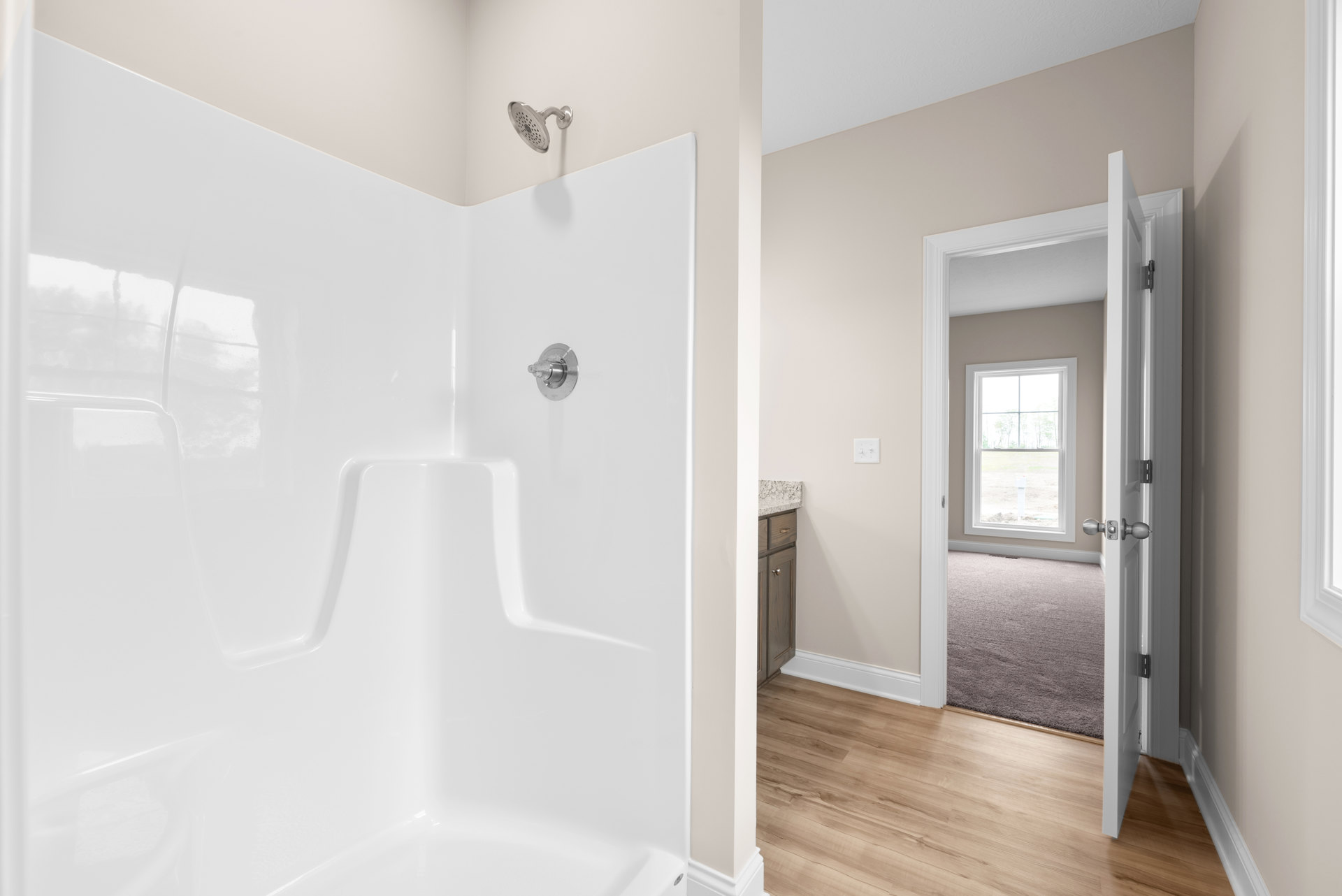 Bathroom featuring a glass-enclosed shower, wood plank flooring, white tile walls, chrome shower head, window overlooking a grassy field, and a close-up of a round metal knob on a