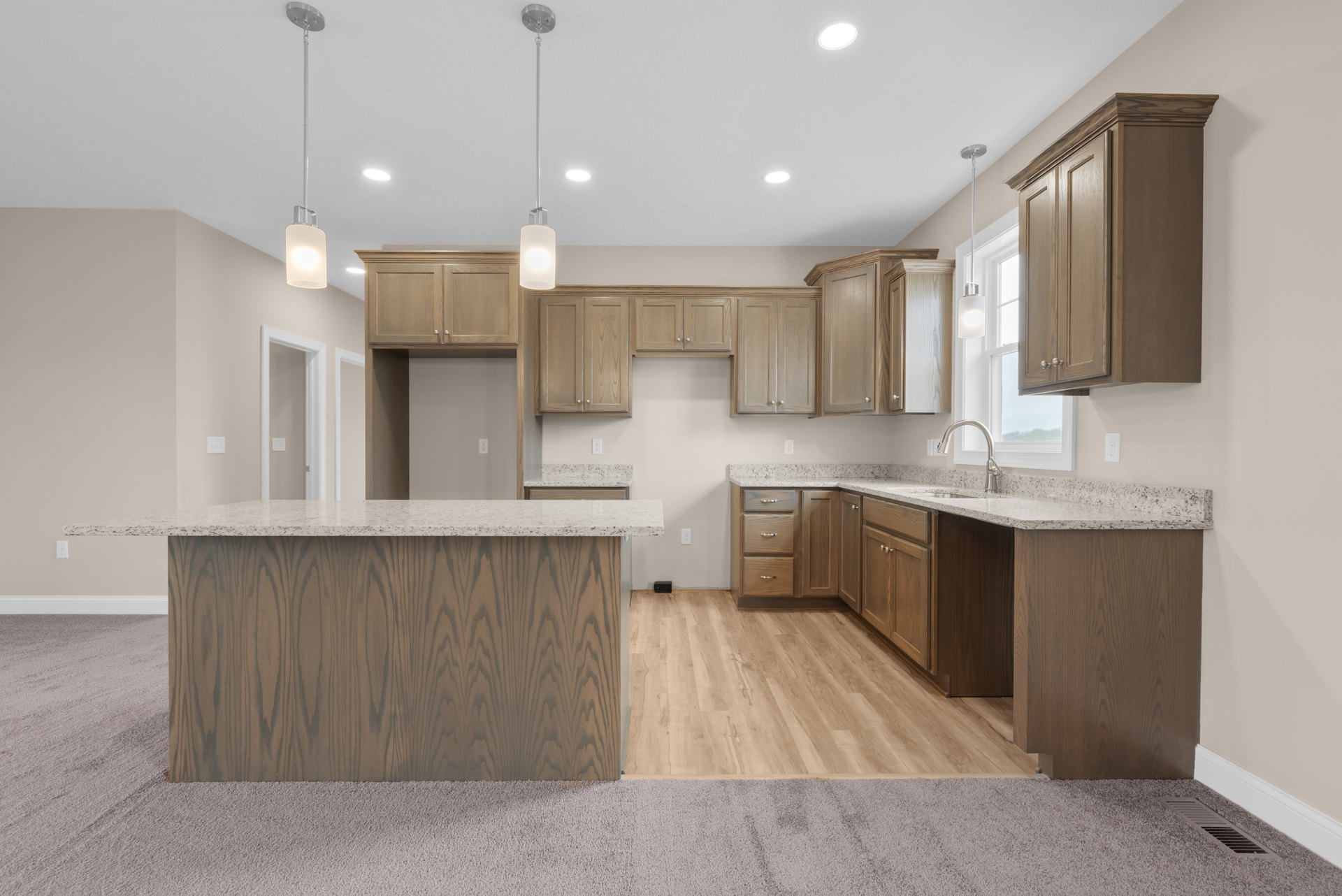 Granite countertops with undermount sink, wood grain flooring, tile backsplash, wooden cabinetry, and recessed lighting in a modern kitchen.