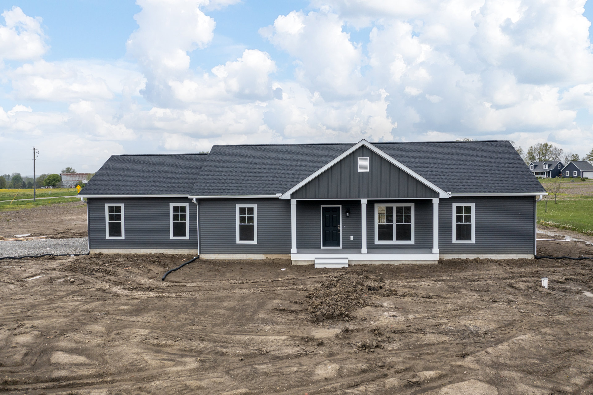 White porch and black door on a partially built house, dirt pile covering front yard, white-framed window, cloudy sky overhead