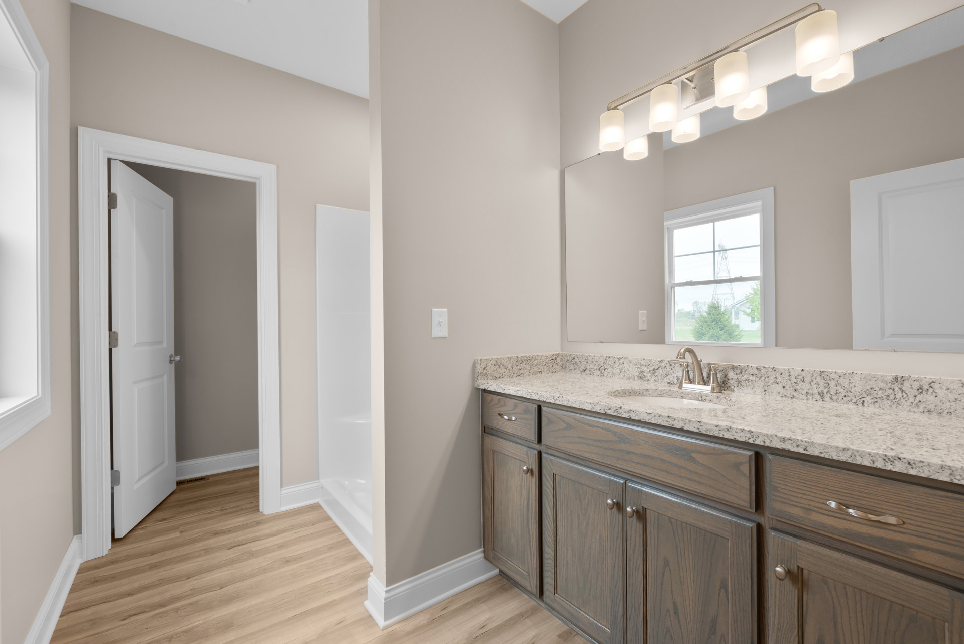 Bathroom featuring marble countertop, glass-enclosed shower, white cabinetry, chrome fixtures, and window with city tower view