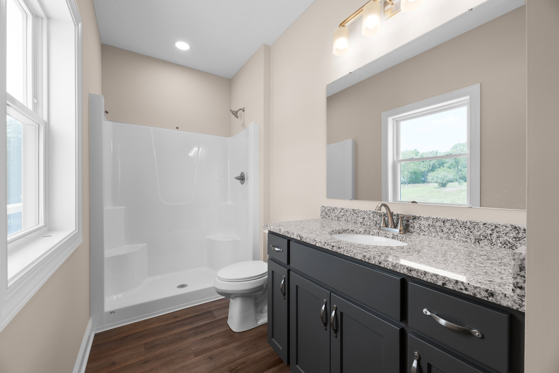 Modern bathroom featuring a white ceramic sink with chrome faucet, light wood cabinetry, tiled walls, glass-enclosed shower, and a window overlooking leafy trees.