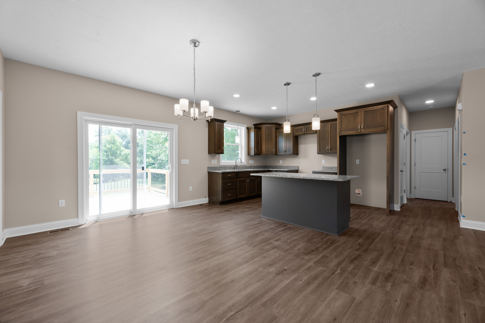 Open kitchen and dining area with wood flooring, marble countertop, white cabinetry, and sliding glass door leading to deck with trees visible outside
