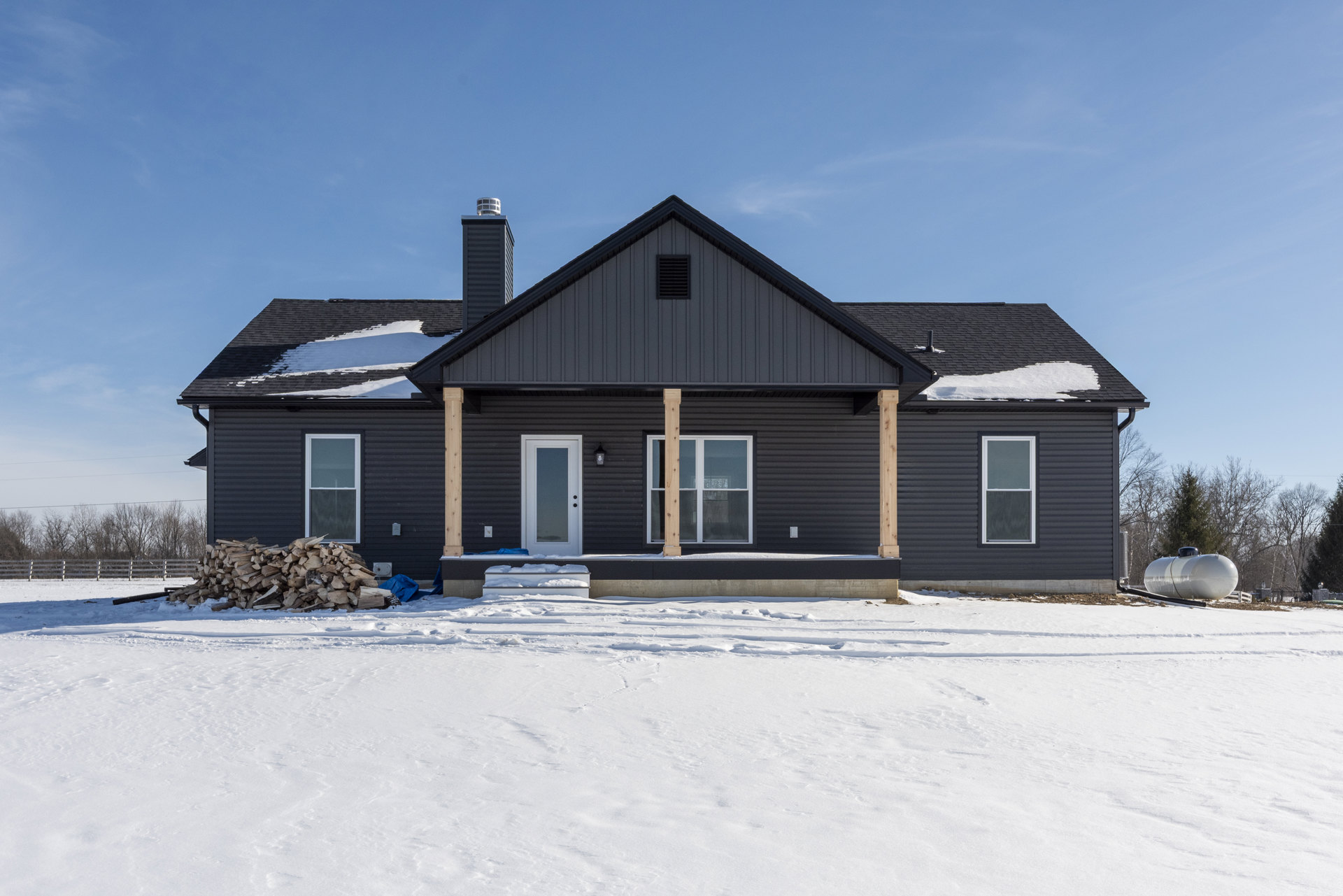 Two-story house with white siding, covered porch, brick chimney, white-framed windows, and snow blanketing the ground and surrounding landscape
