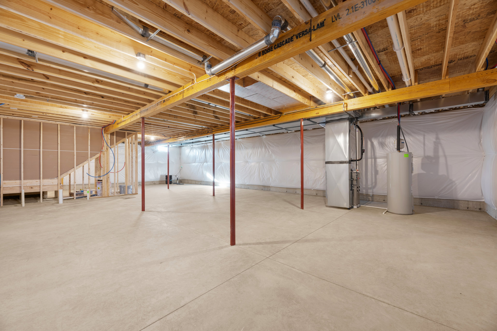 Exposed metal beam and pipes along unfinished ceiling, large white cylinder with blue lid, white rectangular unit with black pipes, concrete floor with red support poles, bare