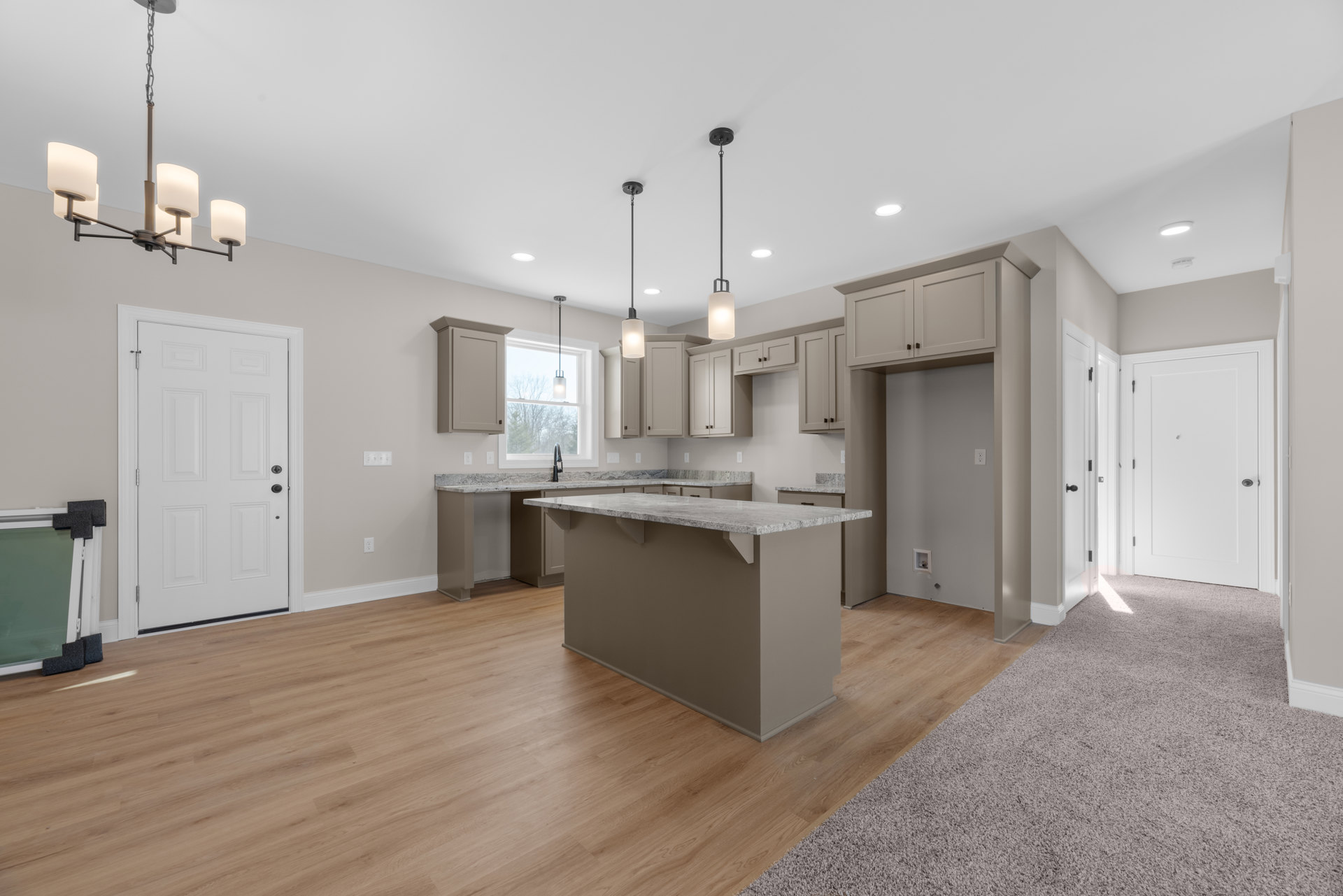 Open-concept kitchen and living room featuring hardwood flooring, white cabinetry, granite kitchen island countertop, white doors with black handles, and modern light fixture.