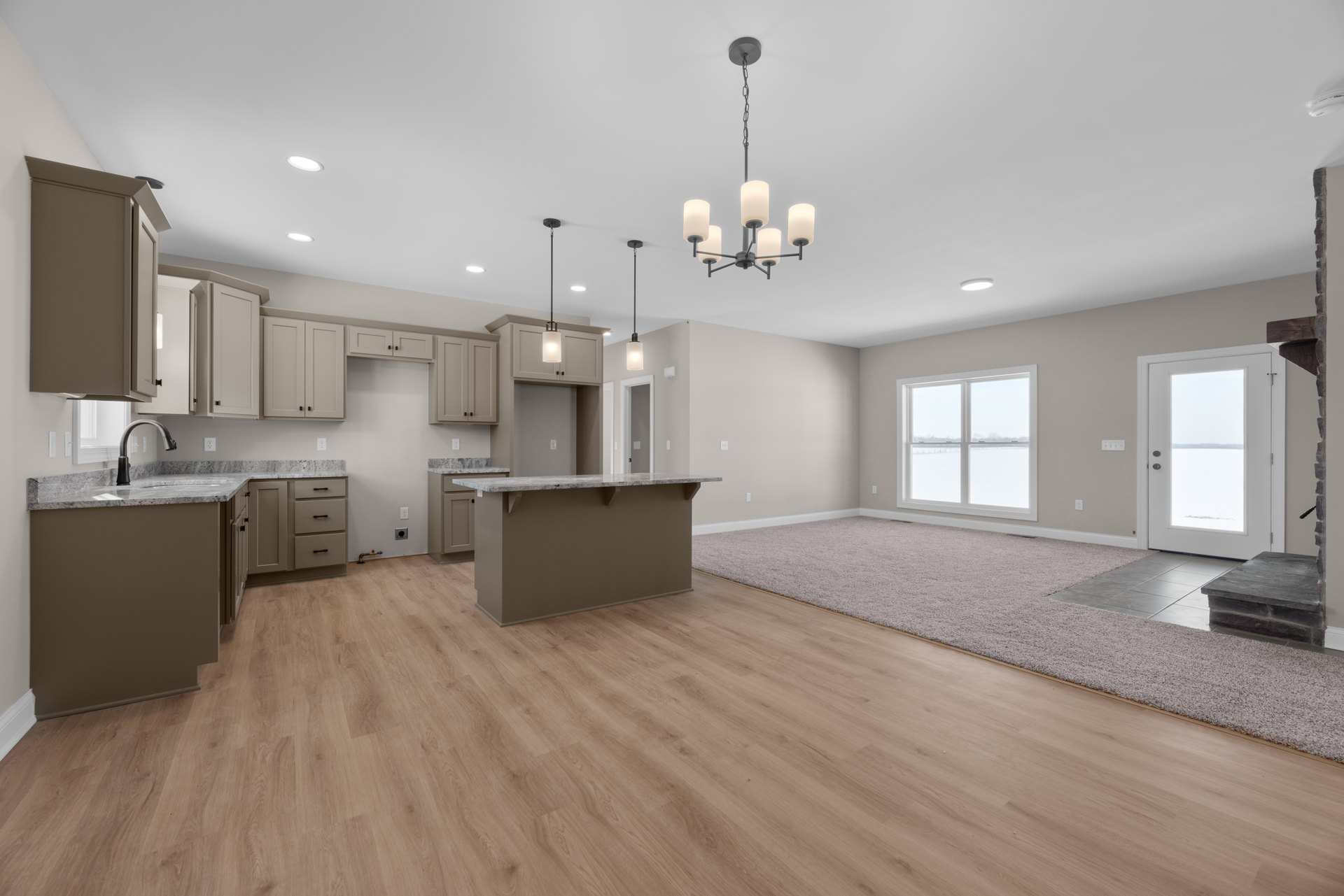 Open kitchen and living room featuring hardwood floors, white cabinetry, stone countertop, stainless steel appliances, large window and door overlooking snowy landscape, dining