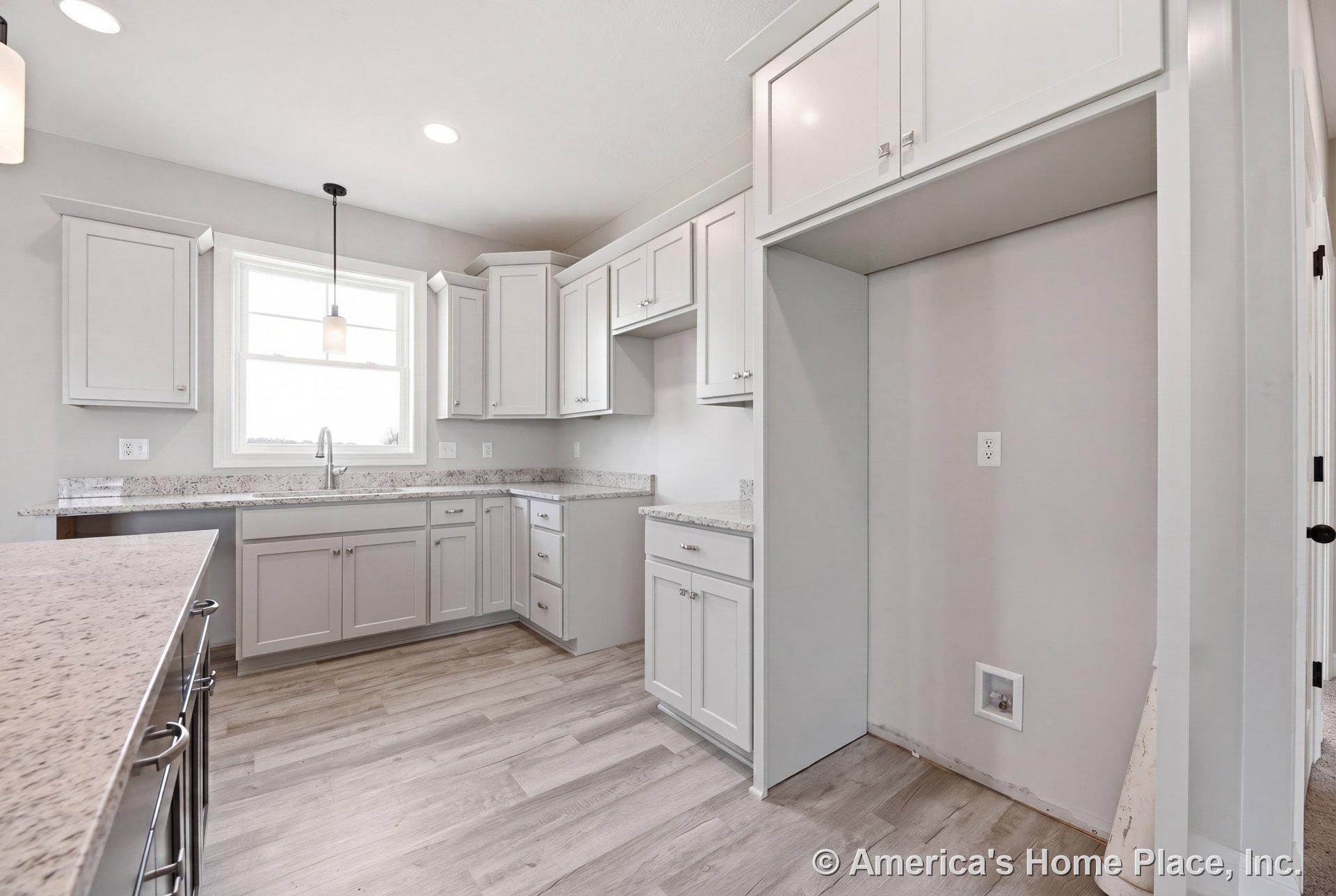 White shaker cabinets with brushed hardware, granite countertops, large window above stainless sink, pendant and recessed lighting, light wood plank flooring, built-in appliance