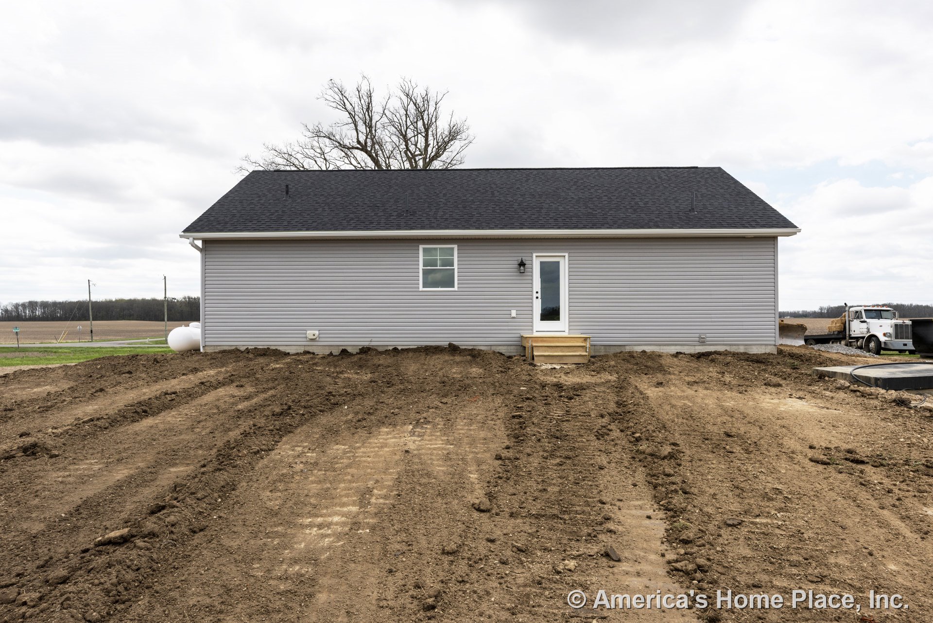 Gray vinyl siding exterior with black shingle roof, single window, rear entry door, small wooden stoop, white trim, and wall-mounted light fixture.