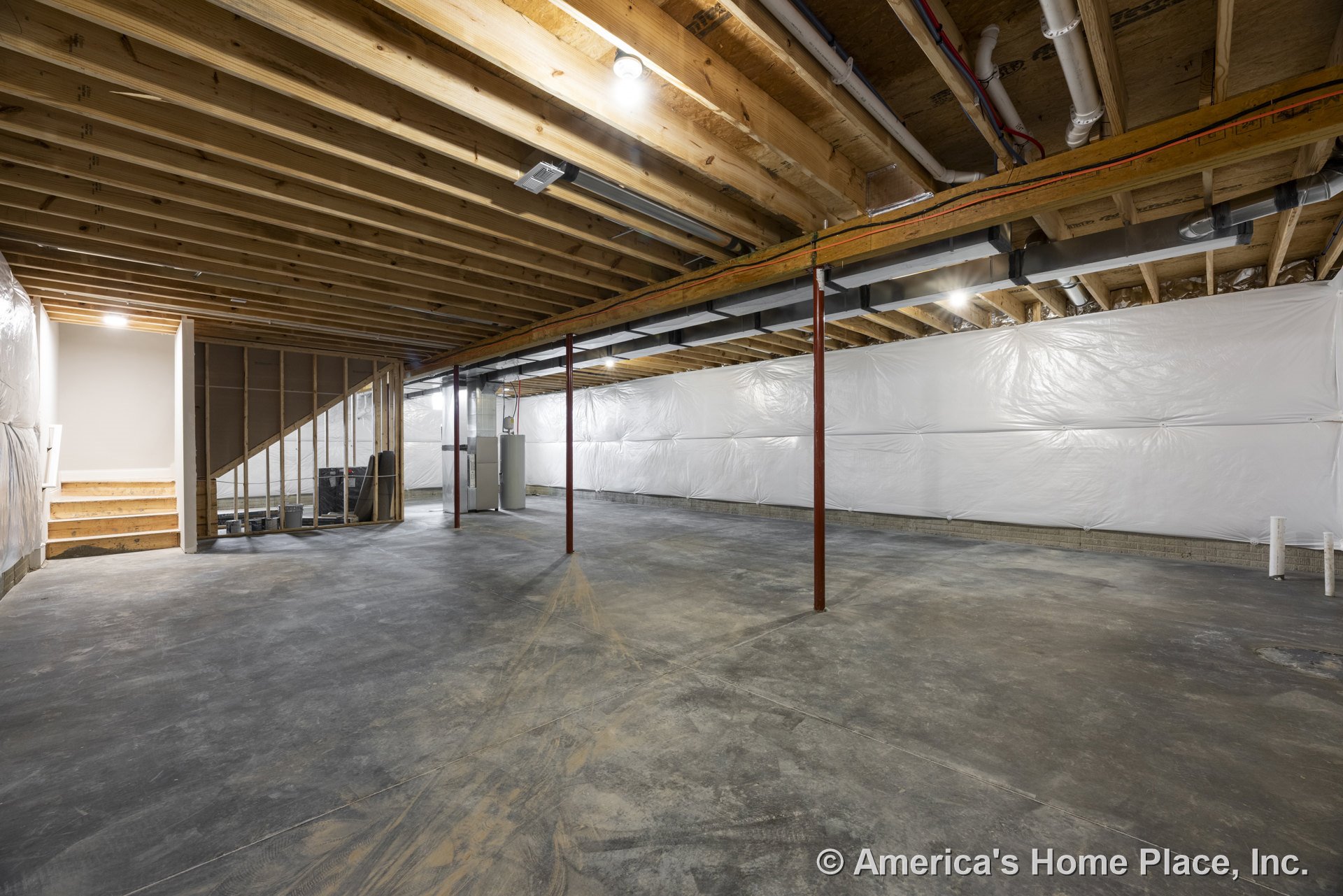 Unfinished basement with exposed wood ceiling joists, concrete slab floor, insulated walls with vapor barriers, open stairway with wood steps, metal support columns, and visible