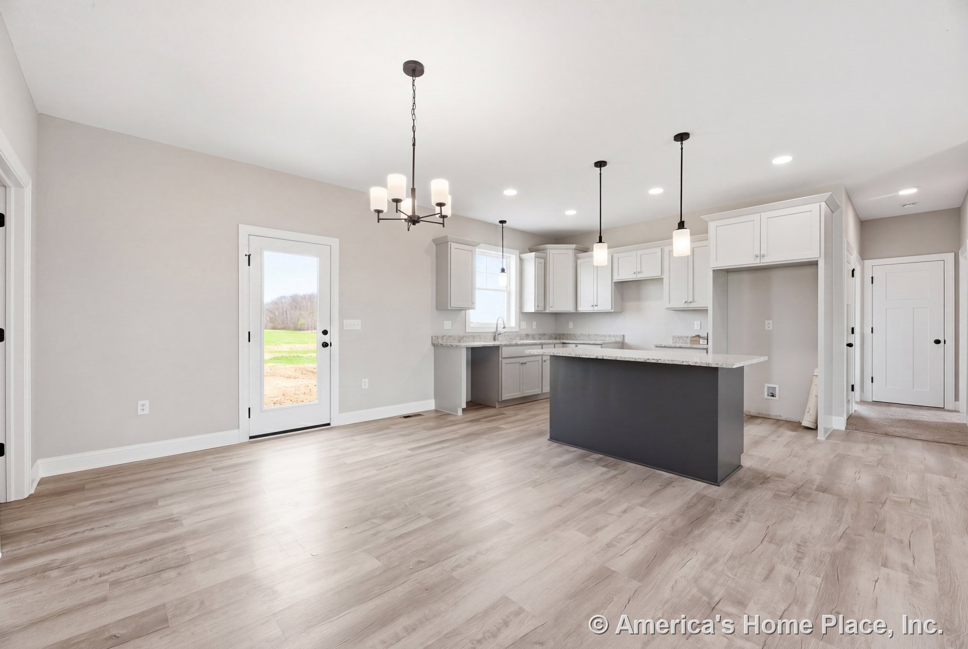 Open kitchen with white shaker cabinets, large stone countertop island, pendant and chandelier lighting, light wood flooring, neutral walls, recessed lighting, and glass exterior
