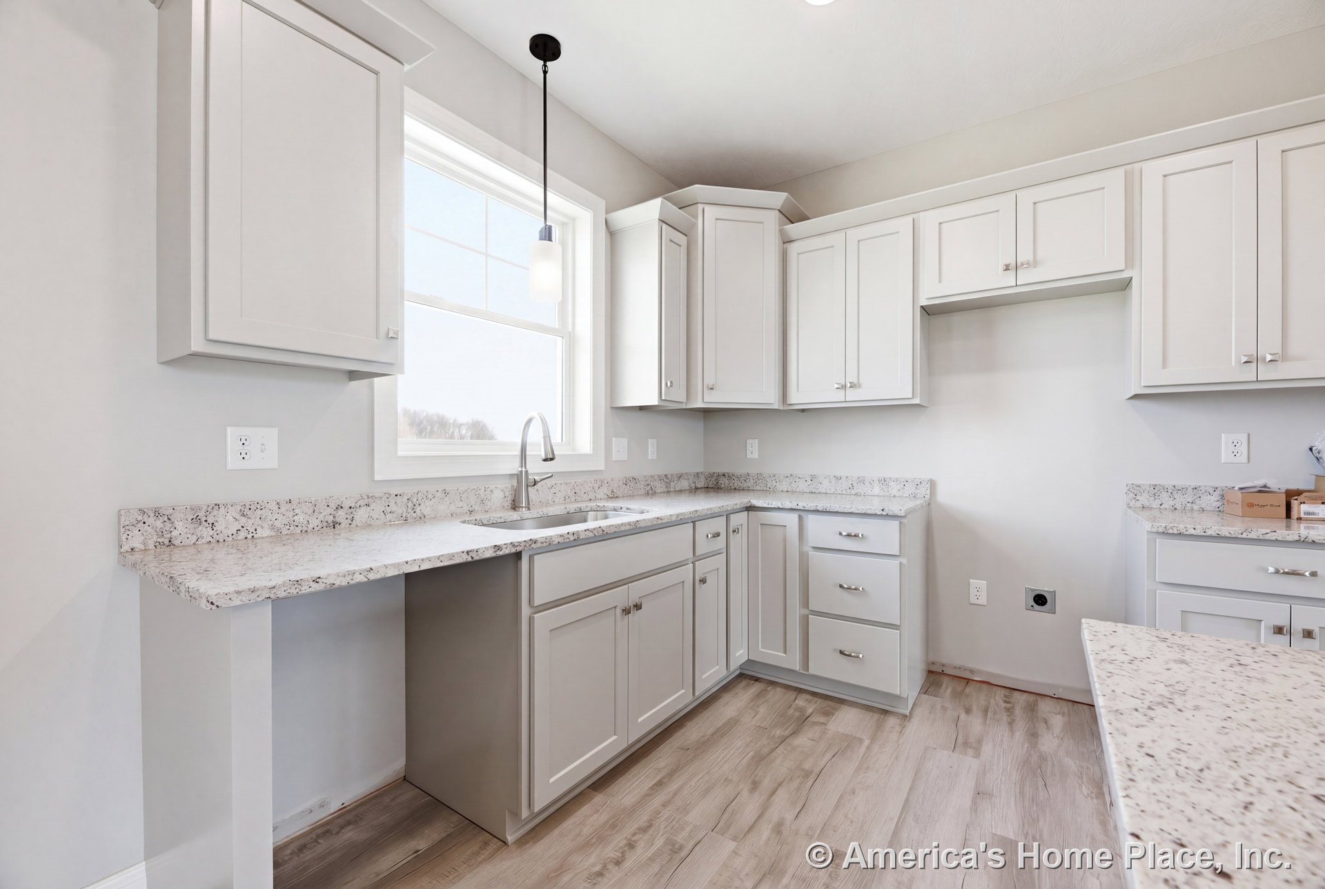 Light gray shaker cabinets with built-in hardware, speckled granite countertops, large window above the sink, pendant light fixture, and wood-look flooring.