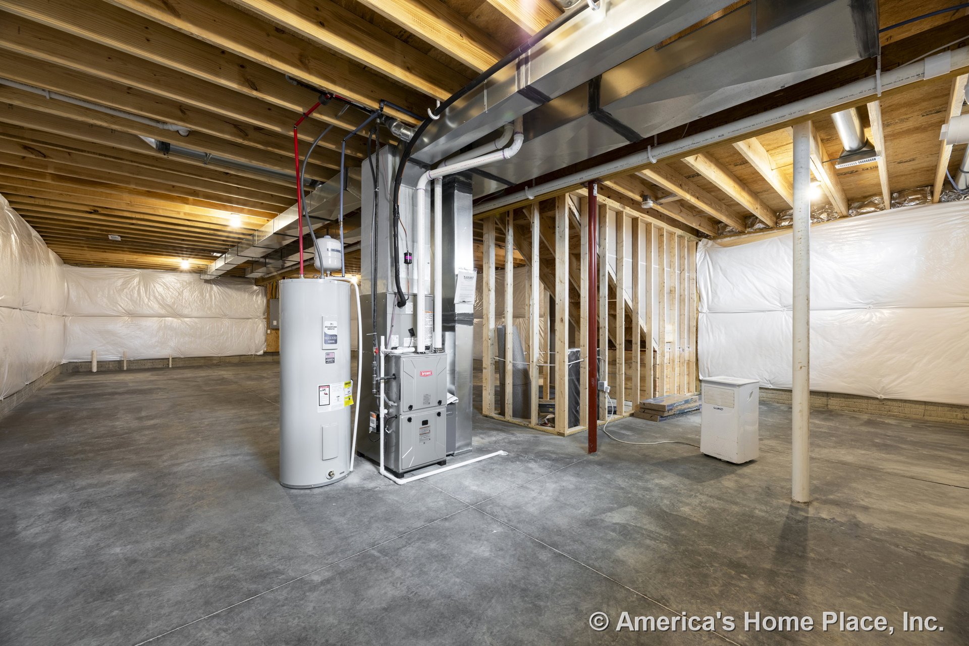 Unfinished basement with exposed wood ceiling joists, concrete slab floor, framed partition wall, installed HVAC unit and water heater tank, plastic vapor barrier on walls, and