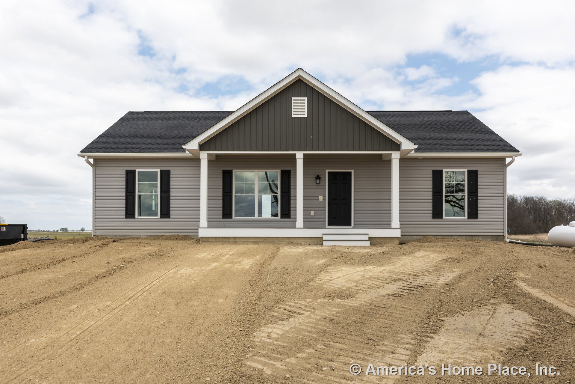Gray vinyl siding exterior with black shutters, double-hung windows, and a covered front porch supported by white columns; dark shingle gable roof, entry door with porch light, and