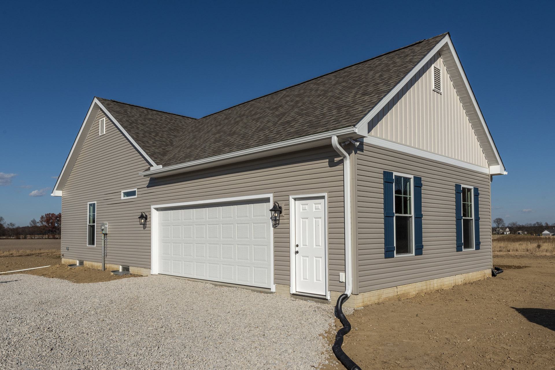 Brown siding house with white garage door, white front door, blue shuttered window, driveway, garden hose on ground