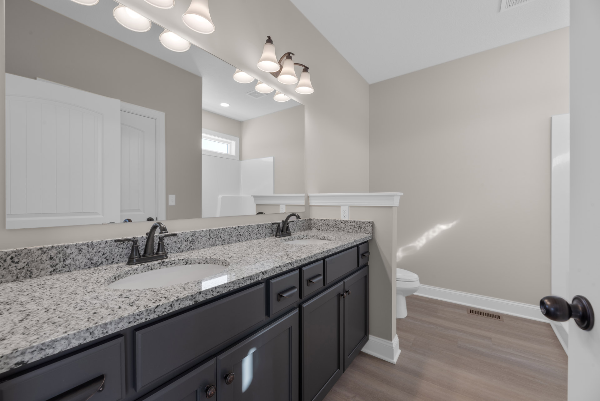 Bathroom with marble countertop, rectangular mirror above sink, white cabinetry, chrome faucet, light fixture with white shade, and partial view of toilet.