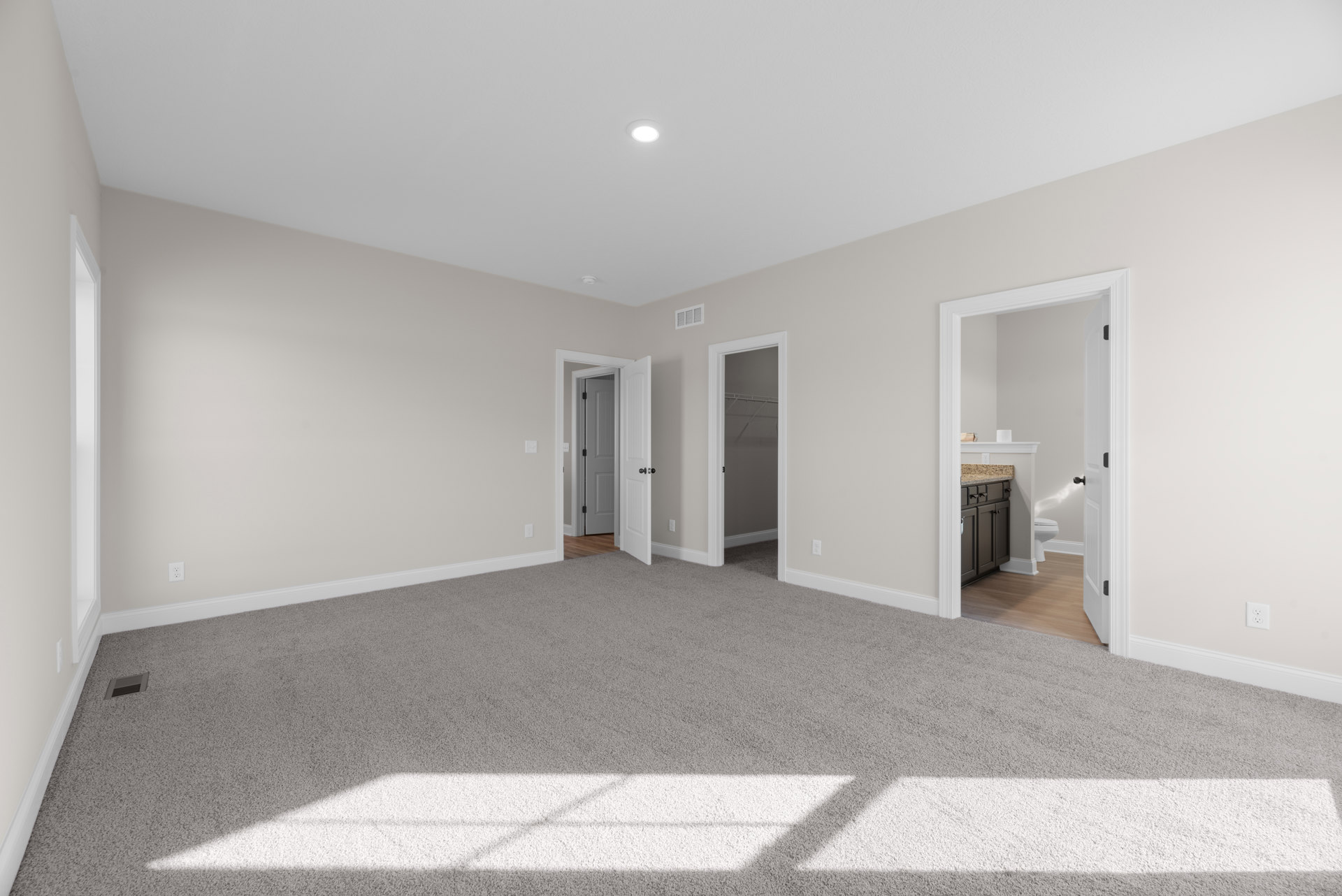 Carpeted room with white walls, open white door with black handle, view into bathroom featuring toilet and sink, close-up of white cabinet