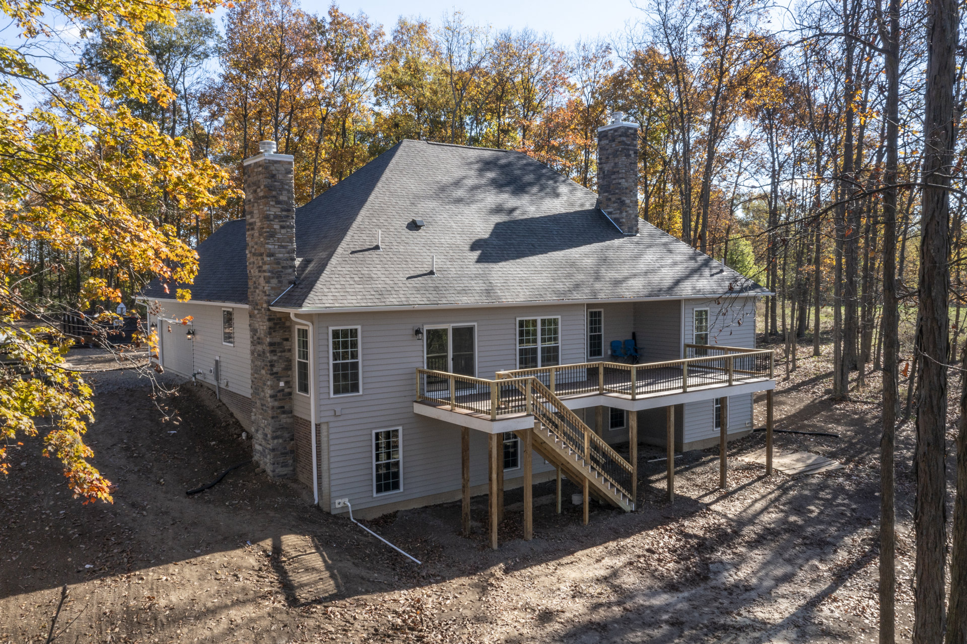 Two-story cottage with multi-pane windows, brick chimney, wooden deck and stairs with railings, covered porch, surrounded by autumn trees.