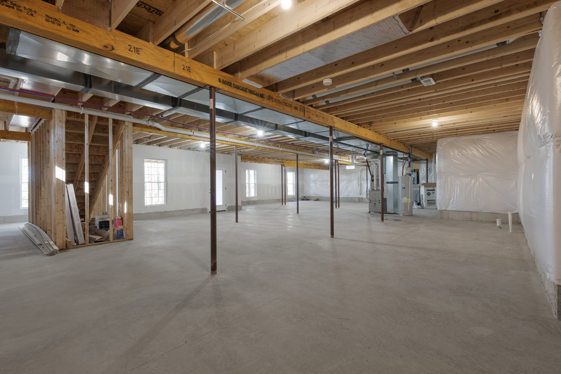 Spacious room with exposed wooden ceiling beams, white plastic wall covering, multi-pane window showing snow outside, metal support poles, and a white door with glass window