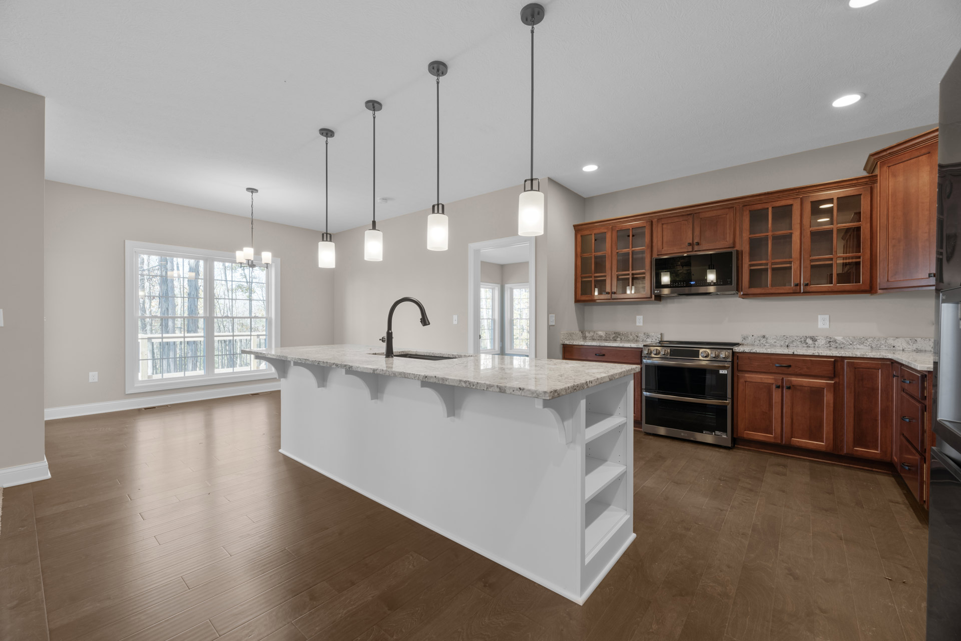 Spacious kitchen featuring a large central island with white countertop, stainless steel stove with black glass door, built-in microwave, undermount sink, light wood cabinetry, and
