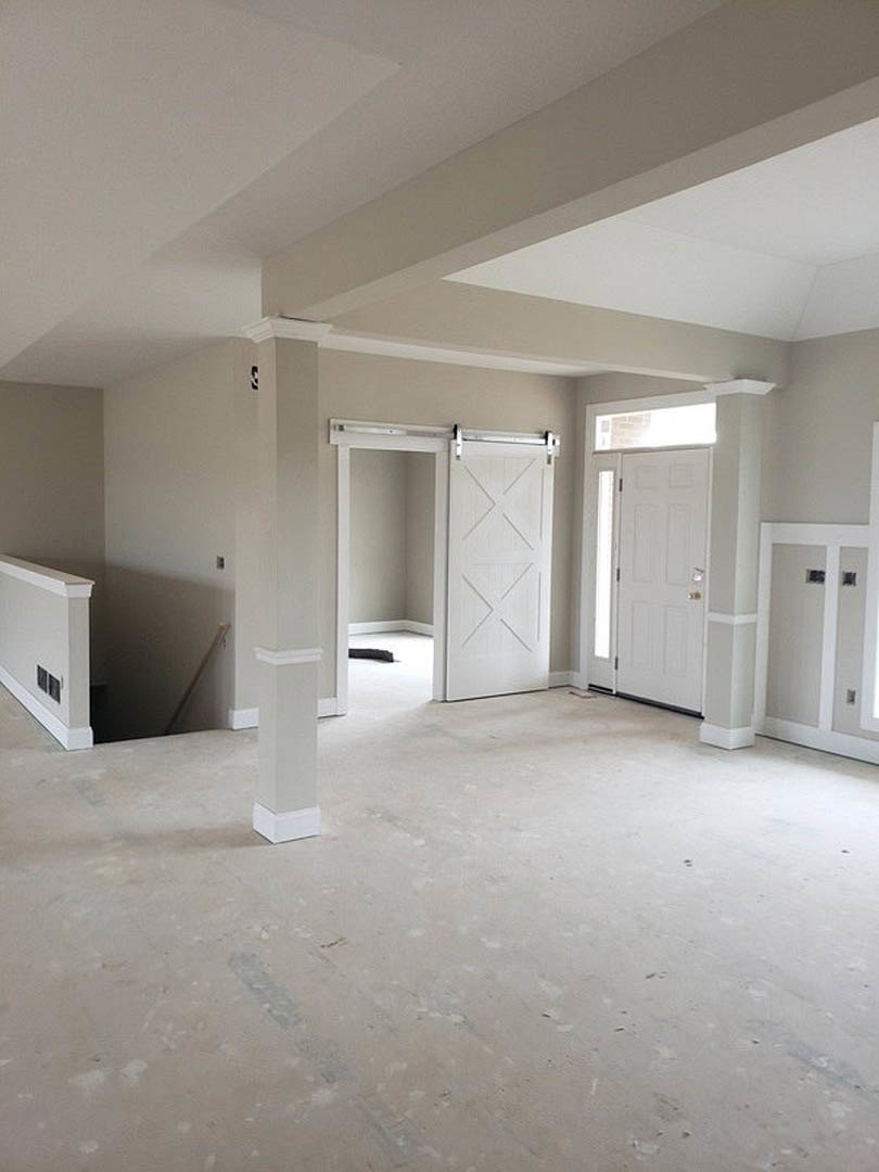 Room with white plaster walls, white columns, white doors featuring gold handles and cross patterns, glass door, wall vent, and light flooring