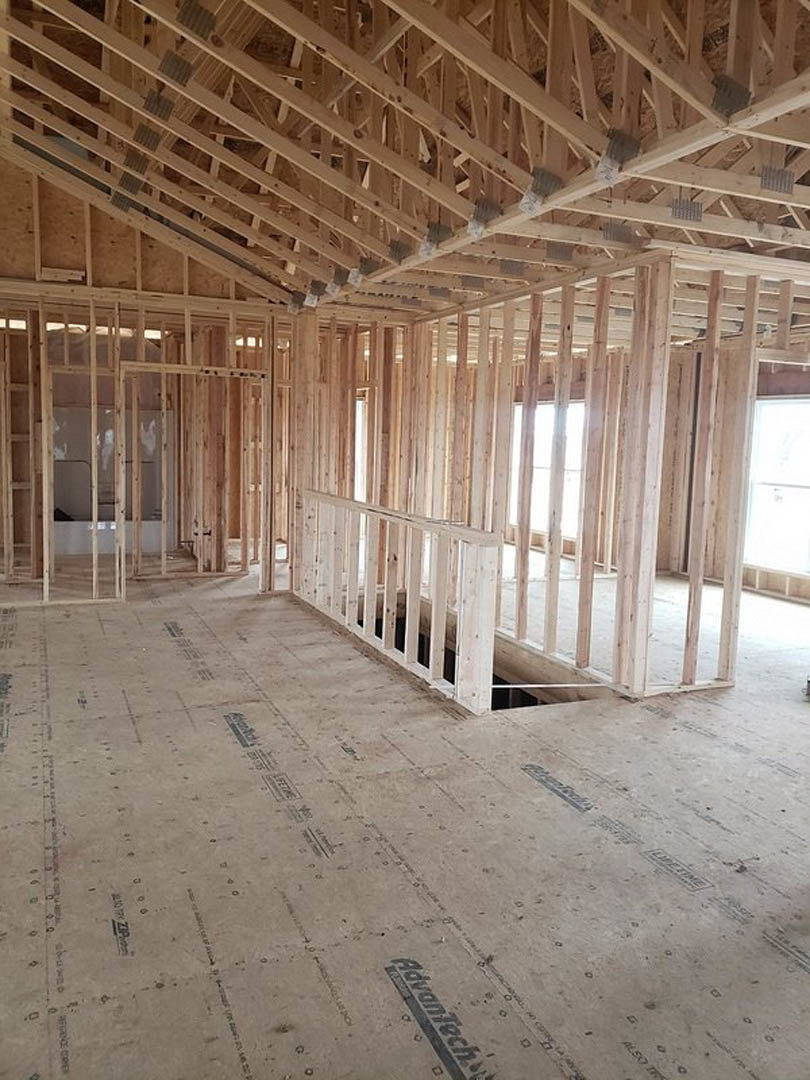 Wood-framed house under construction with exposed beams, unfinished walls, and a white window illuminated by sunlight