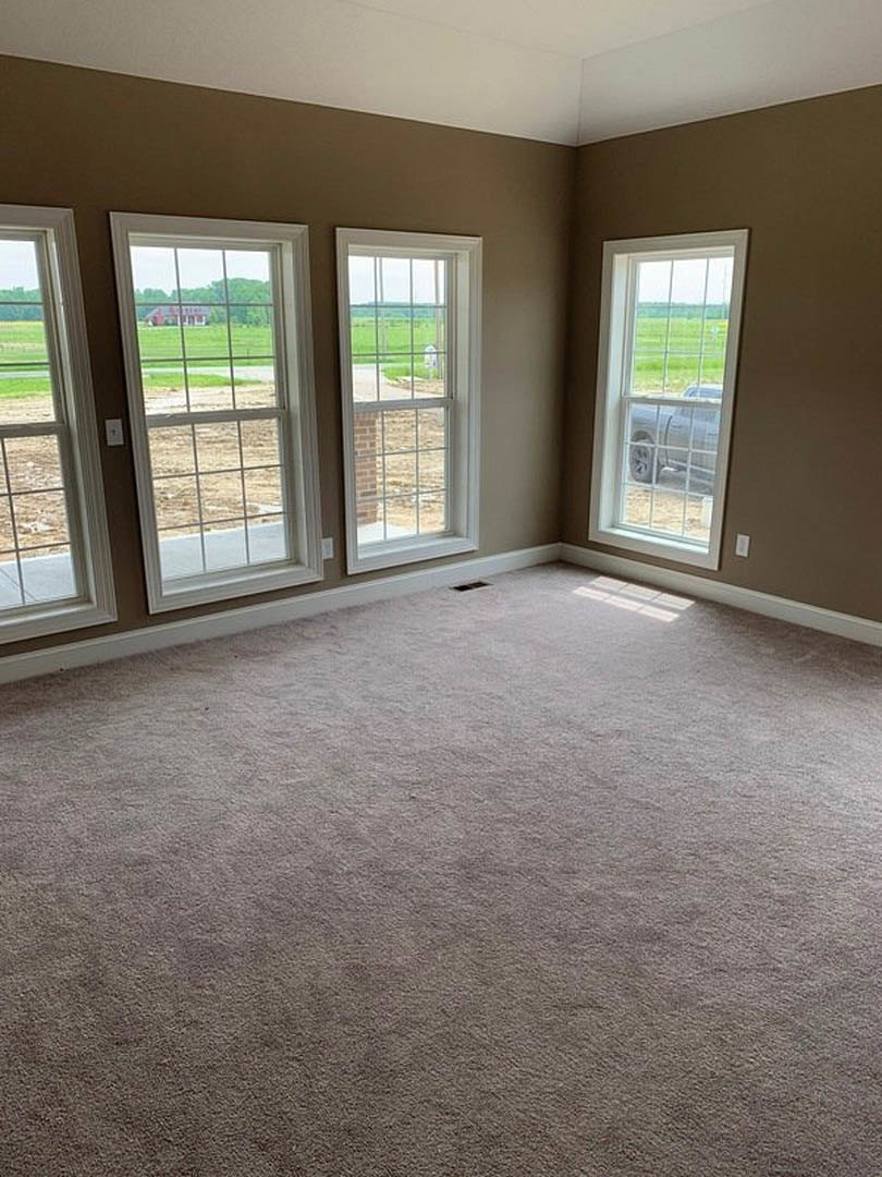 Carpeted room with multiple windows, views of grassy field, brick wall, and parked car outside