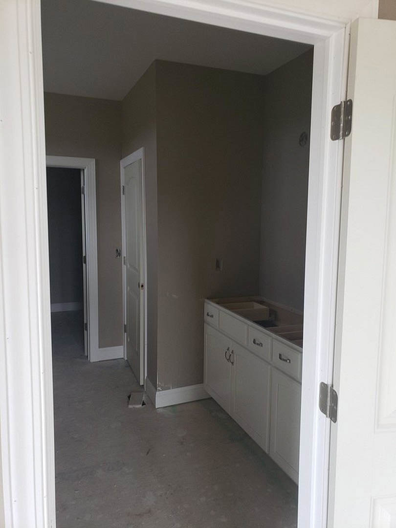White kitchen cabinets with silver handles, white doors, light flooring, and black door with white frame