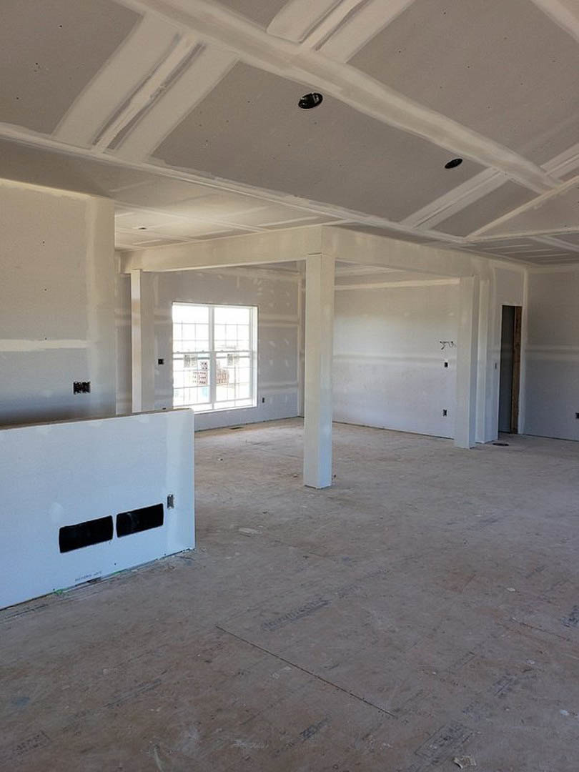Room with smooth white plaster walls, large window with black rectangular frames, light-colored composite flooring, ceiling featuring recessed holes.
