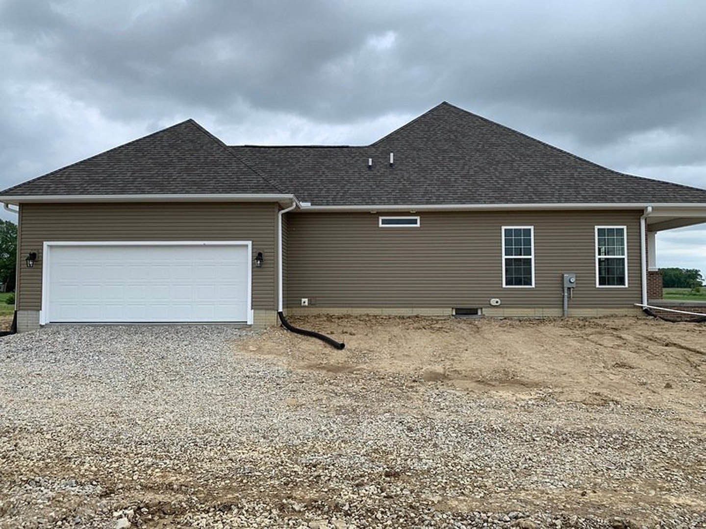 White garage door with black frame, white-framed window, gray siding, asphalt driveway, dark shingle roof, metal vent pipe, partly cloudy sky
