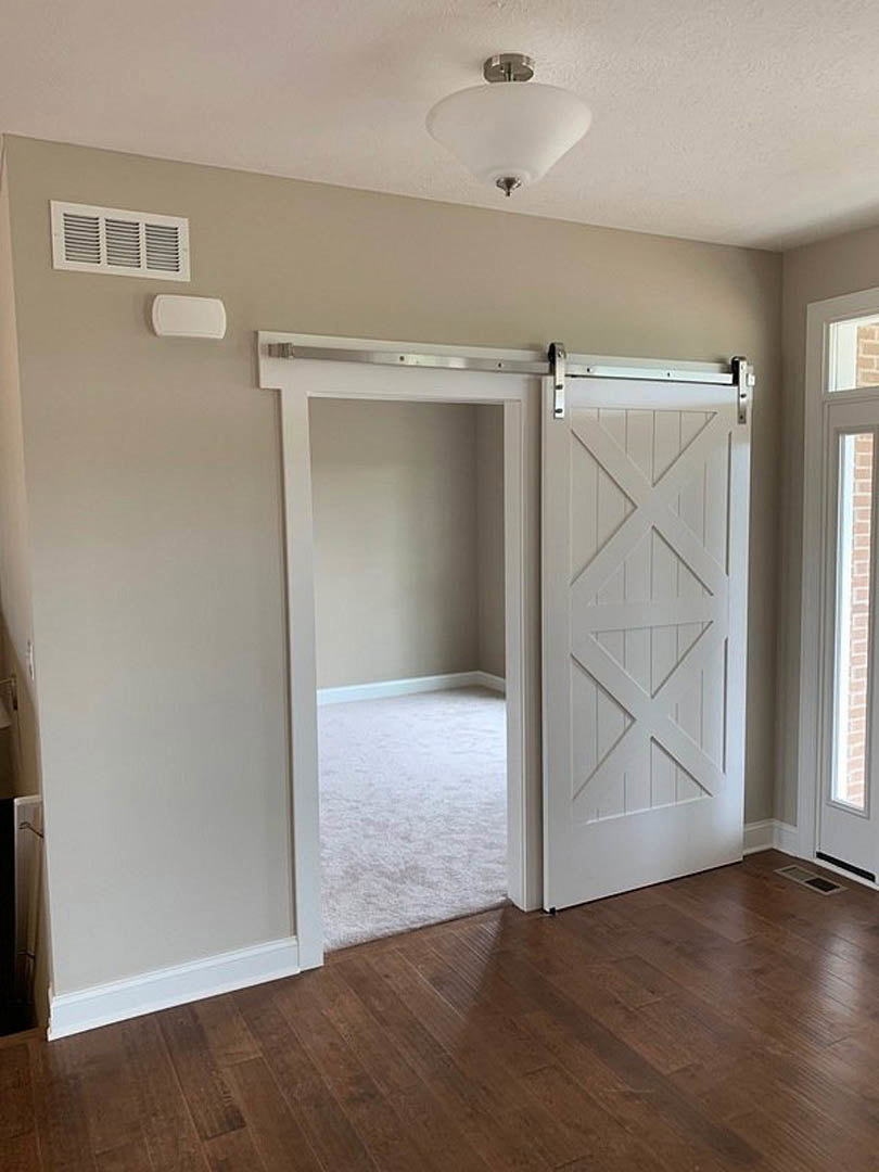 Sliding glass door with black trim, white cross-patterned door, wooden laminate flooring, wall vent, ceiling light fixture, plaster walls