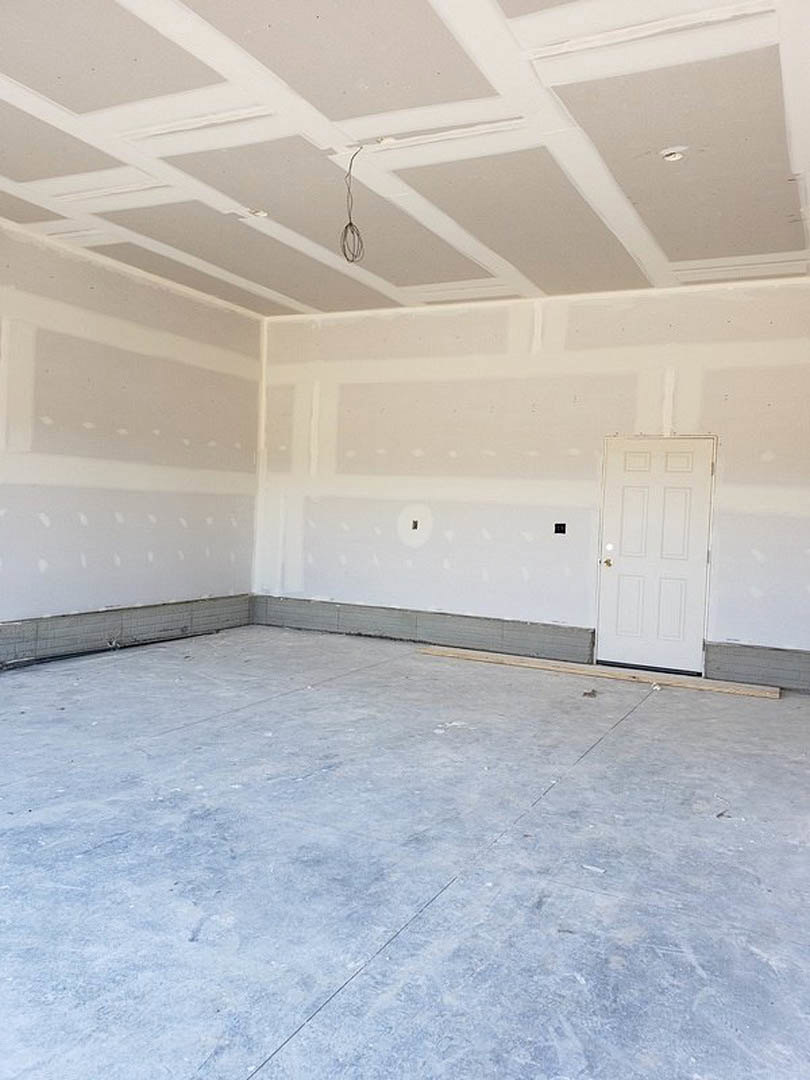 White walls and ceiling, white door with gold handle, exposed wire hanging from ceiling, concrete floor with wood plank, person standing near wall
