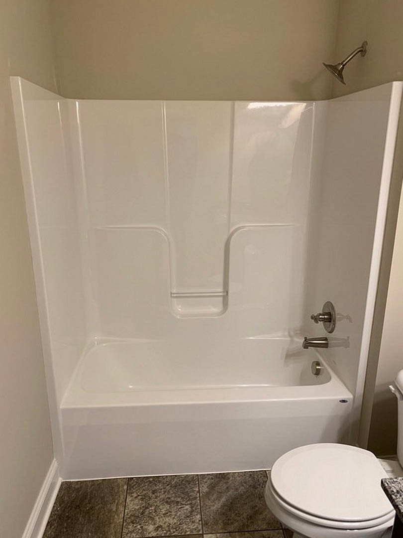 Freestanding white bathtub beside a tiled wall, white toilet with lid up, chrome shower head, close-up of tile flooring and faucet in modern bathroom.