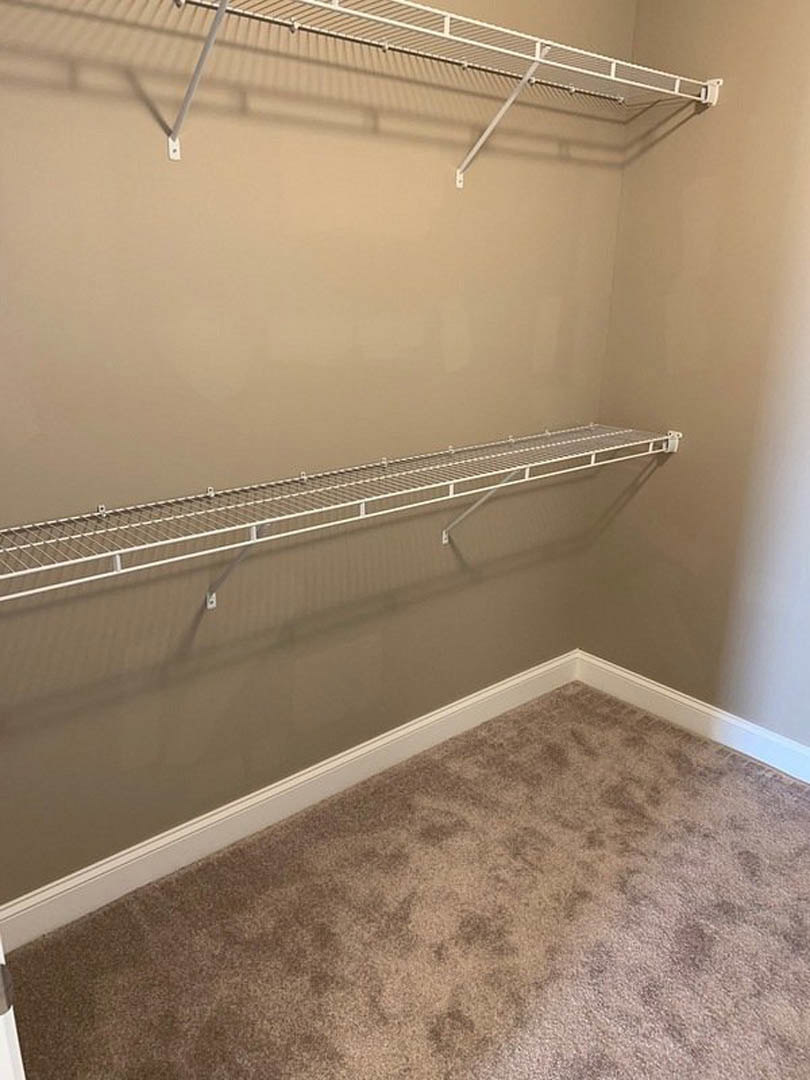 Walk-in closet with white shelving, hanging metal rod, and light-colored carpet flooring
