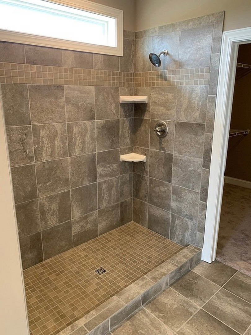 Walk-in shower with two chrome shower heads mounted on tiled wall, marble tile flooring, and linear drain