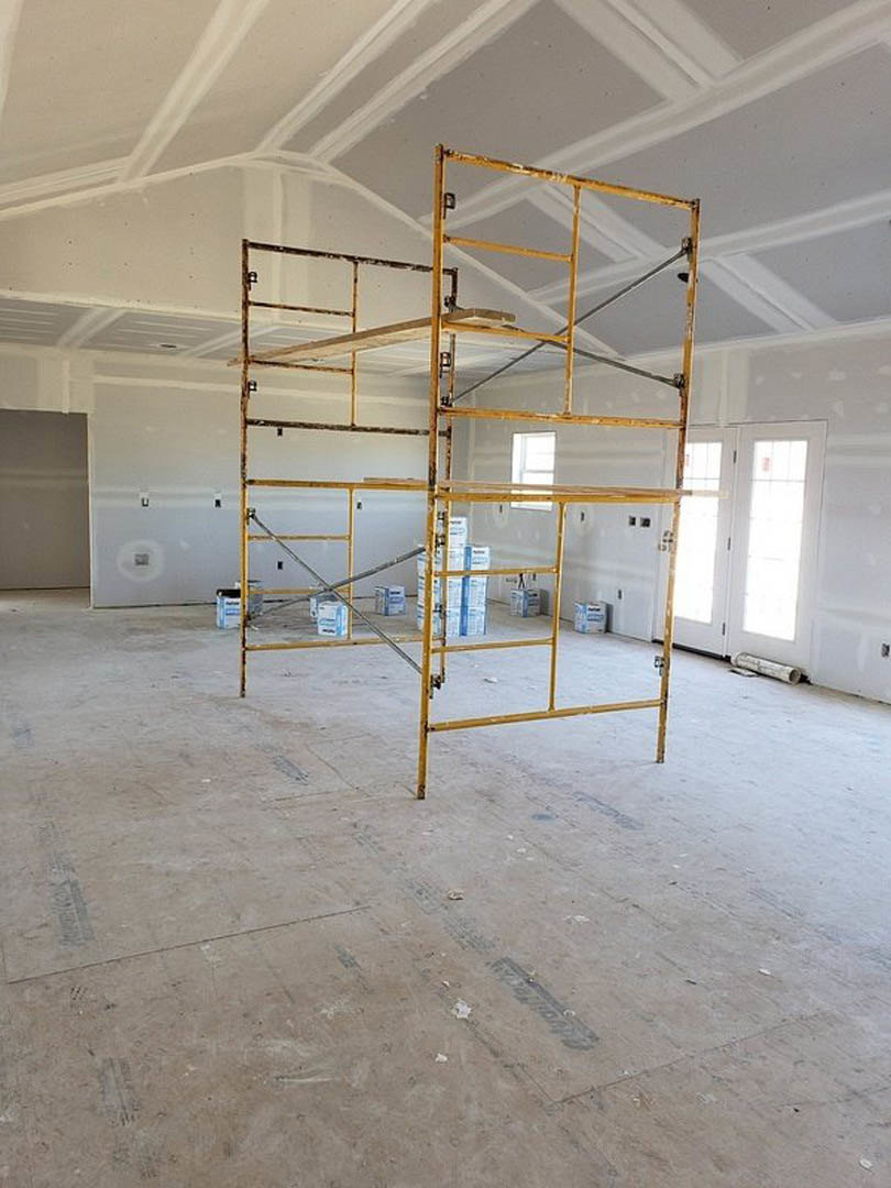Yellow scaffolding with cardboard boxes stands in a room featuring a large window, white walls with black trim, and a white door with a wooden handle illuminated by natural light.