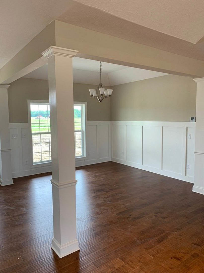 Wood flooring with white pillars, chandelier hanging from ceiling, white walls with windows, white door and trim