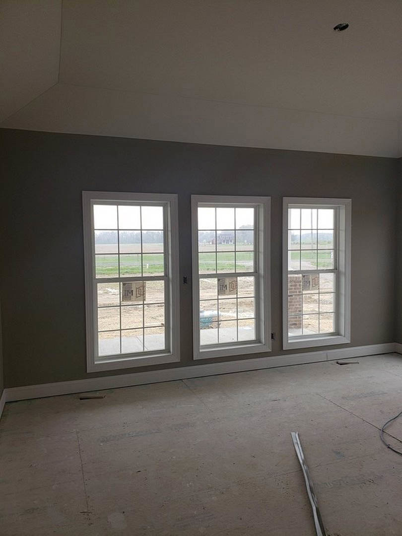Spacious room featuring a row of large windows, smooth concrete flooring, plaster walls, and a brick accent wall.