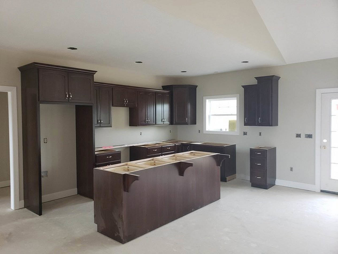 Dark wood kitchen cabinets with silver handles, white-framed window above a light countertop, four-drawer base cabinet, black file cabinet, close-up of door handle and black