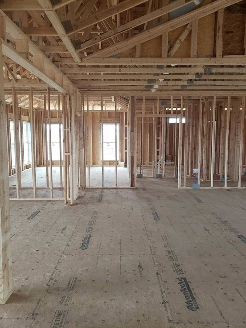 Exposed wood ceiling beams, unfinished walls, large square windows, and construction materials on the floor in a residential interior under construction
